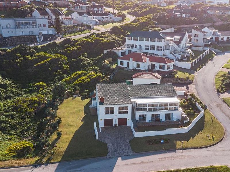 Aerial view of a residential property featuring a tiled roof, paved driveway, double garage, and an enclosed patio area within a coastal neighborhood.