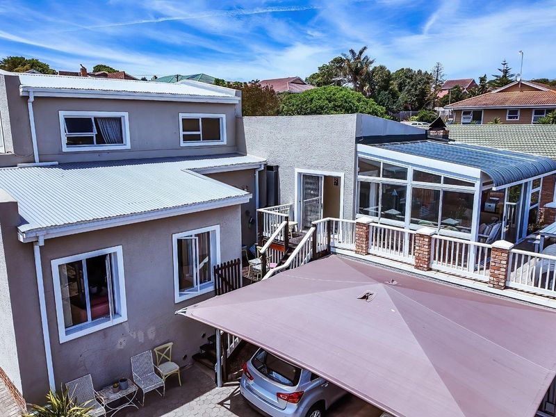 Rear exterior view of the property featuring a raised deck, sunroom, paved driveway area, and carport structure.