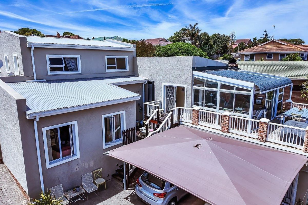 Rear exterior view of the property featuring a raised deck, sunroom, paved driveway area, and carport structure.