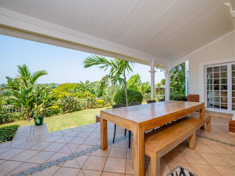 A spacious covered patio featuring tiled flooring with decorative inlays, support columns, and direct access to the garden and scenic views.