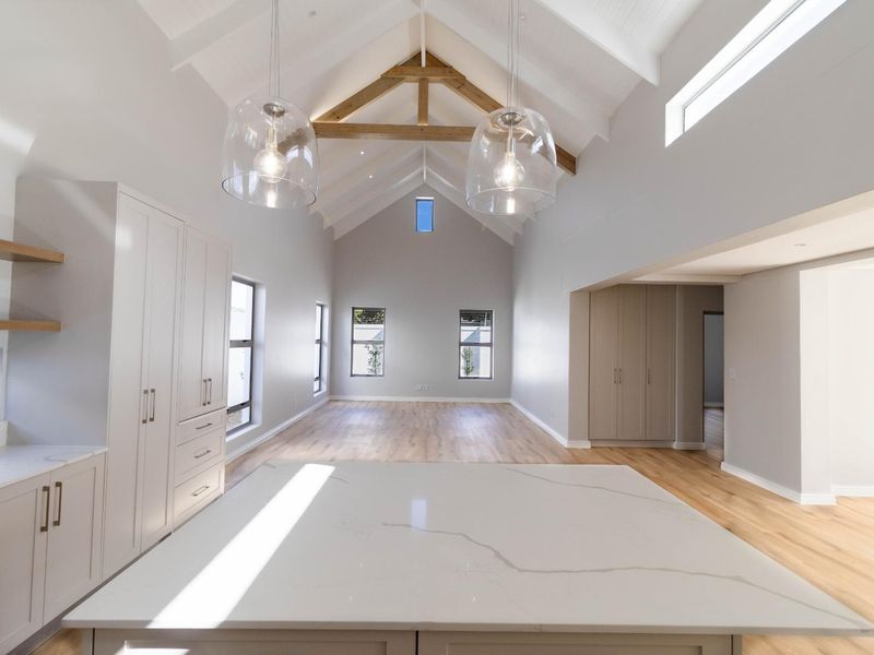 Spacious open-plan living area featuring a dramatic vaulted ceiling with exposed timber trusses, stone kitchen island, and modern neutral finishes throughout.