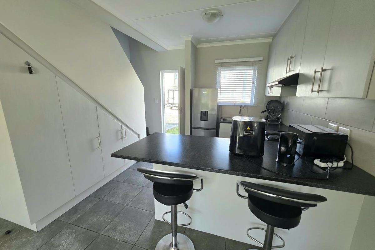 Modern kitchen featuring built-in cabinetry, a breakfast bar with stone countertops, and efficient under-stair storage, finished with neutral tones and tiled flooring.