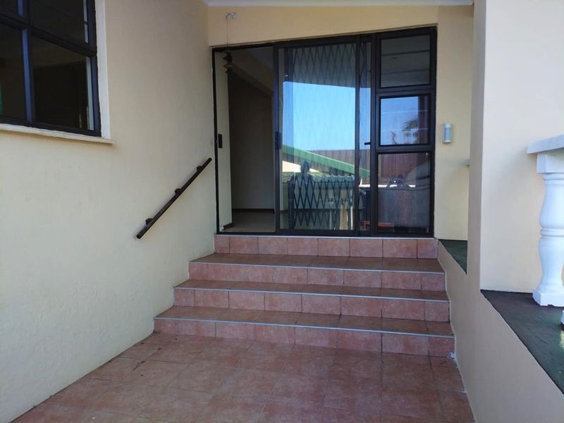 Entrance area featuring tiled steps leading to a sliding glass door with a security gate and wall-mounted handrail.