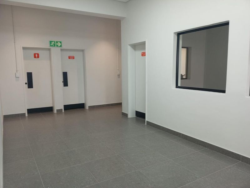 A clean, modern industrial hallway featuring grey tiled flooring, white walls, and multiple access doors with clear signage.
