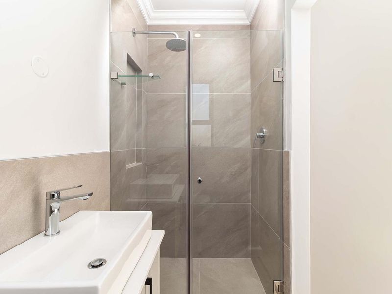 Modern bathroom featuring a glass-enclosed shower with a rain shower head, contemporary vanity basin, and neutral large-format wall tiles.