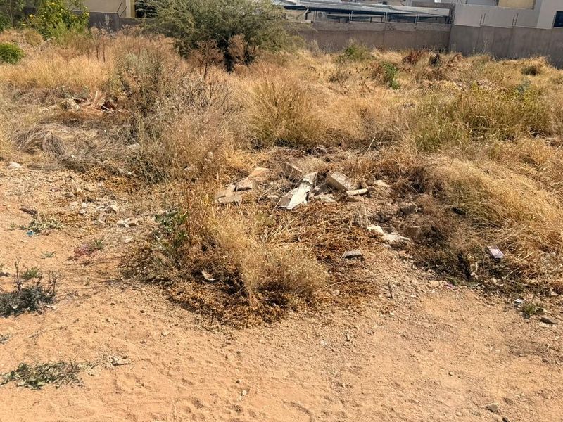 A view of the vacant residential land featuring dry, overgrown vegetation and scattered debris across the plot.