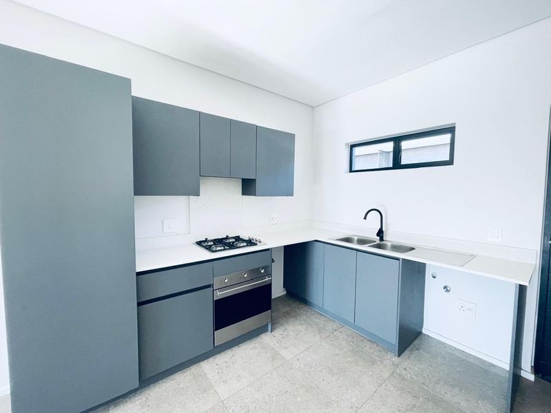 Modern kitchen featuring grey cabinetry, stone countertops, gas hob, built-in oven, and a double sink with a contemporary black mixer tap.