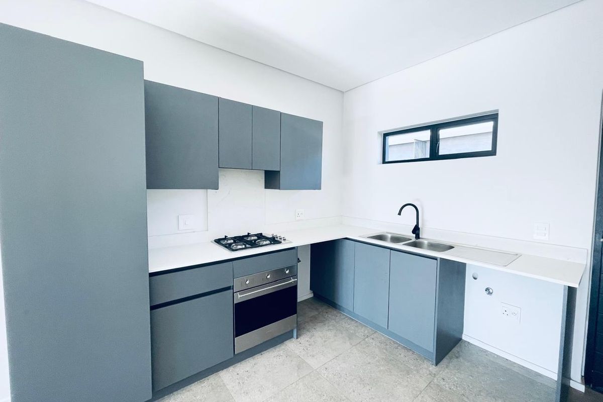 Modern kitchen featuring grey cabinetry, stone countertops, gas hob, built-in oven, and a double sink with a contemporary black mixer tap.