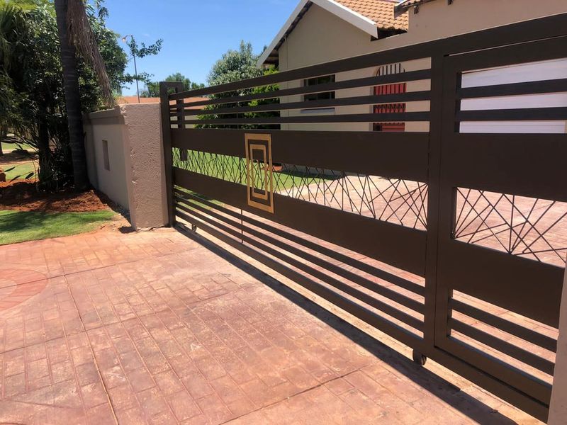 A modern sliding driveway gate with decorative metalwork, leading to a paved driveway and the front entrance of the house.