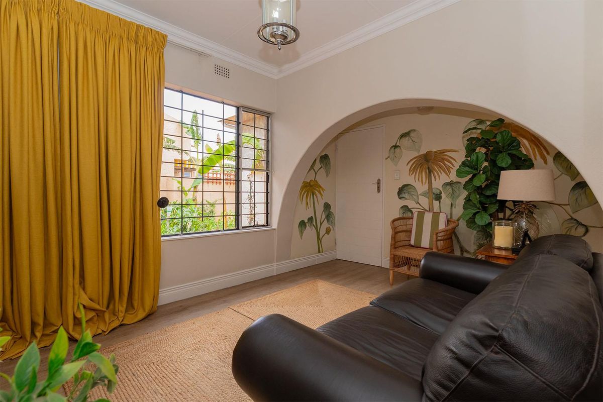 A cozy living room featuring a distinctive arched wall alcove with decorative mural, large window with security bars, and crown molding.