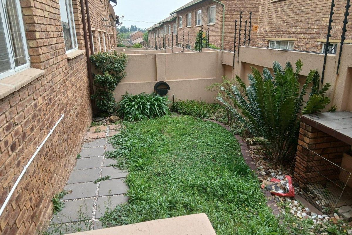 A private rear garden area featuring a brick boundary wall with electric fencing, a paved walkway, and a built-in brick braai facility.