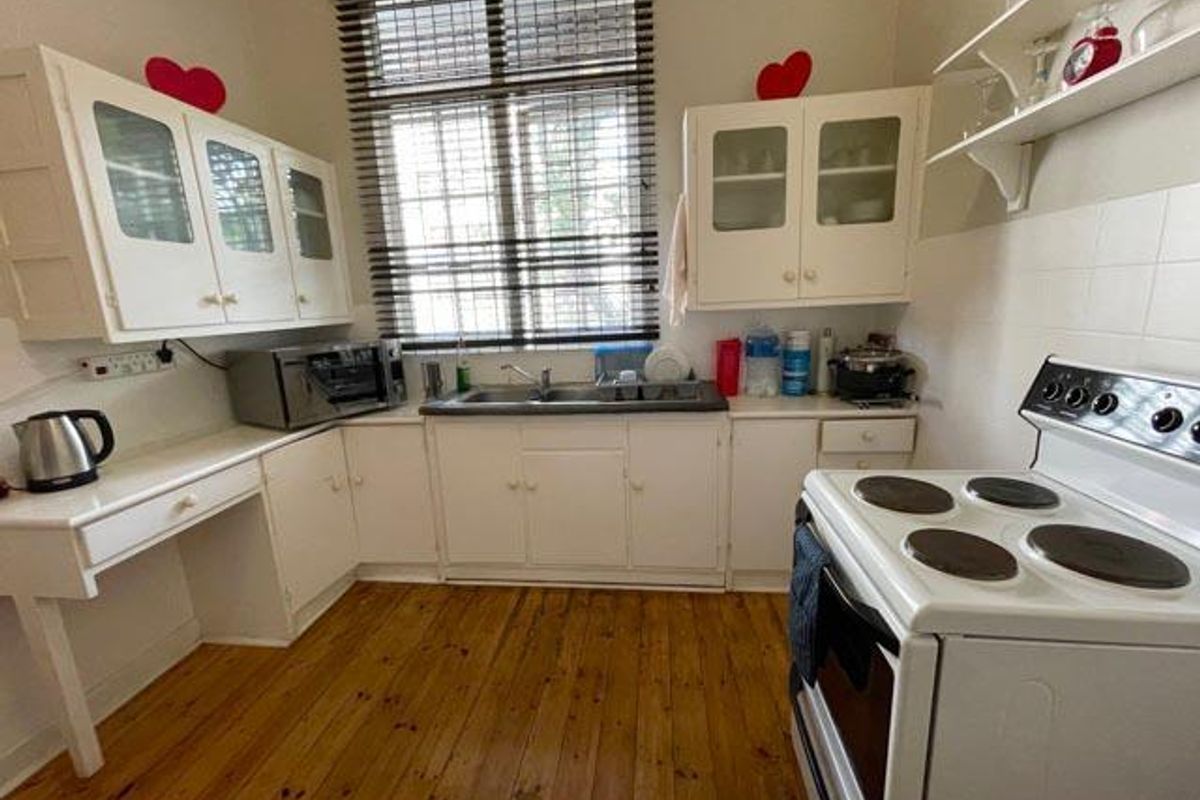 A functional kitchen featuring white cabinetry, timber flooring, a freestanding electric stove, and a double-basin sink with a window view.