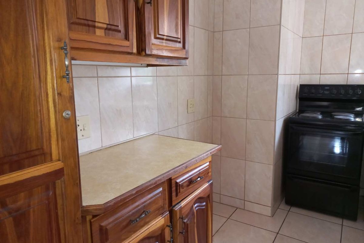 A functional kitchen area featuring traditional wooden cabinetry, tiled splashbacks, and a freestanding black electric stove.