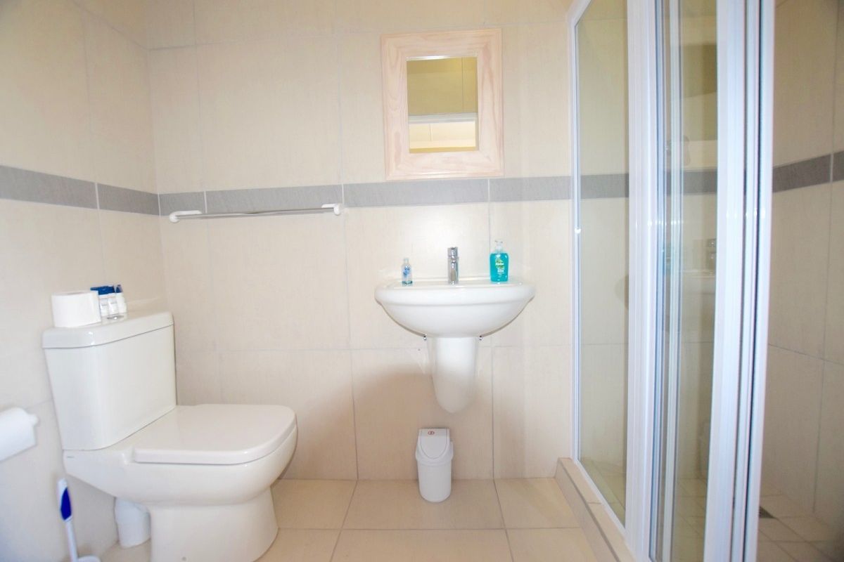 A functional bathroom featuring a pedestal basin, a standard toilet, and a glass-enclosed shower with neutral wall and floor tiling.