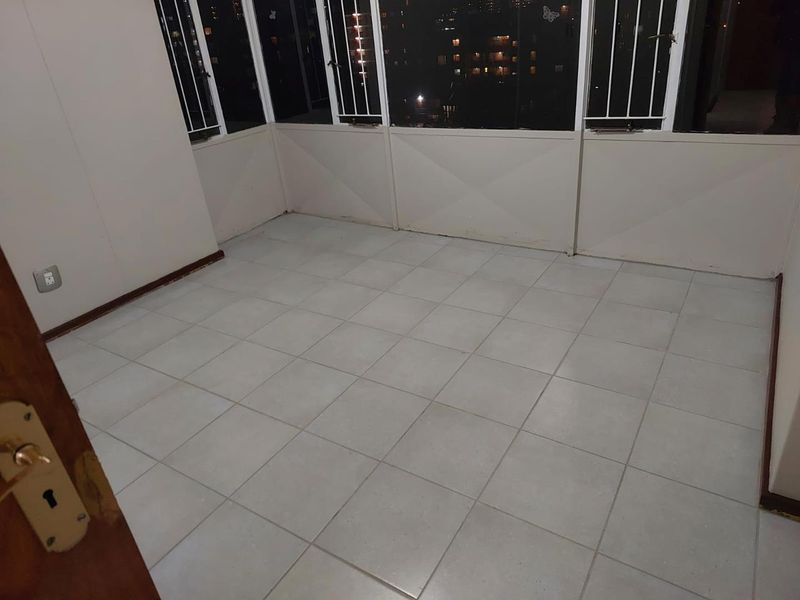 An enclosed balcony or sunroom featuring tiled flooring and large windows with security bars, offering an elevated view of the surrounding area.