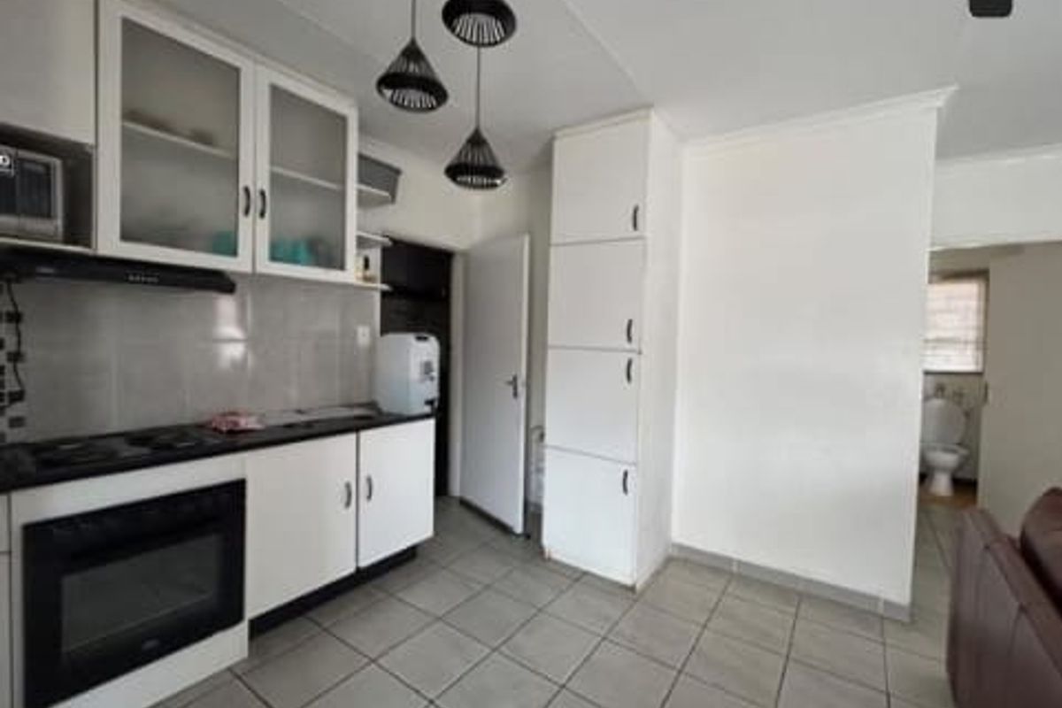 A functional kitchen featuring white cabinetry, a built-in oven with extractor fan, tiled flooring, and a tall pantry cupboard.