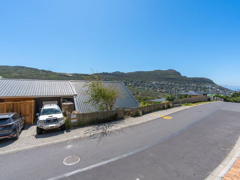 Street view of the property showing the paved driveway, metal roof structure, and surrounding hillside landscape.