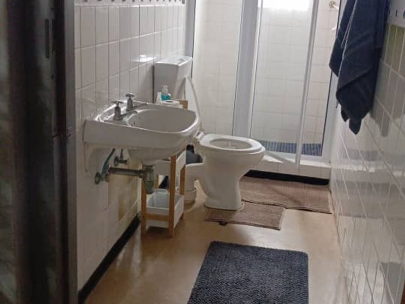 A functional bathroom featuring a wall-mounted basin, toilet, and a separate shower enclosure with white tiled walls.