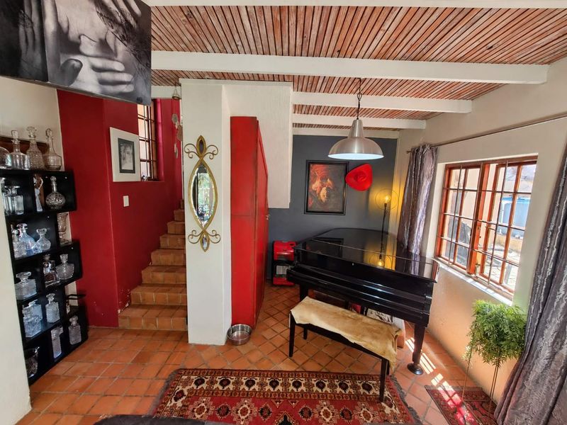 Living area featuring a timber-slat ceiling with exposed beams, terracotta floor tiles, and a staircase leading to the upper level.