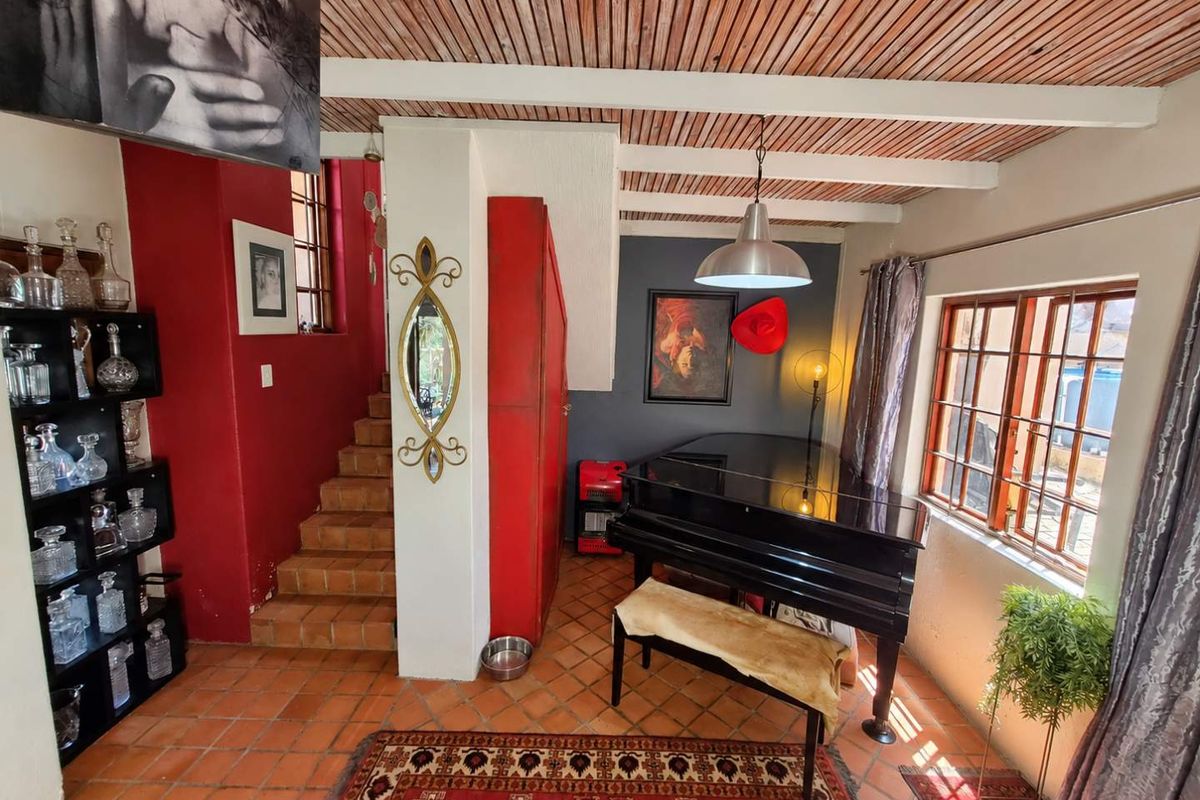 Living area featuring a timber-slat ceiling with exposed beams, terracotta floor tiles, and a staircase leading to the upper level.