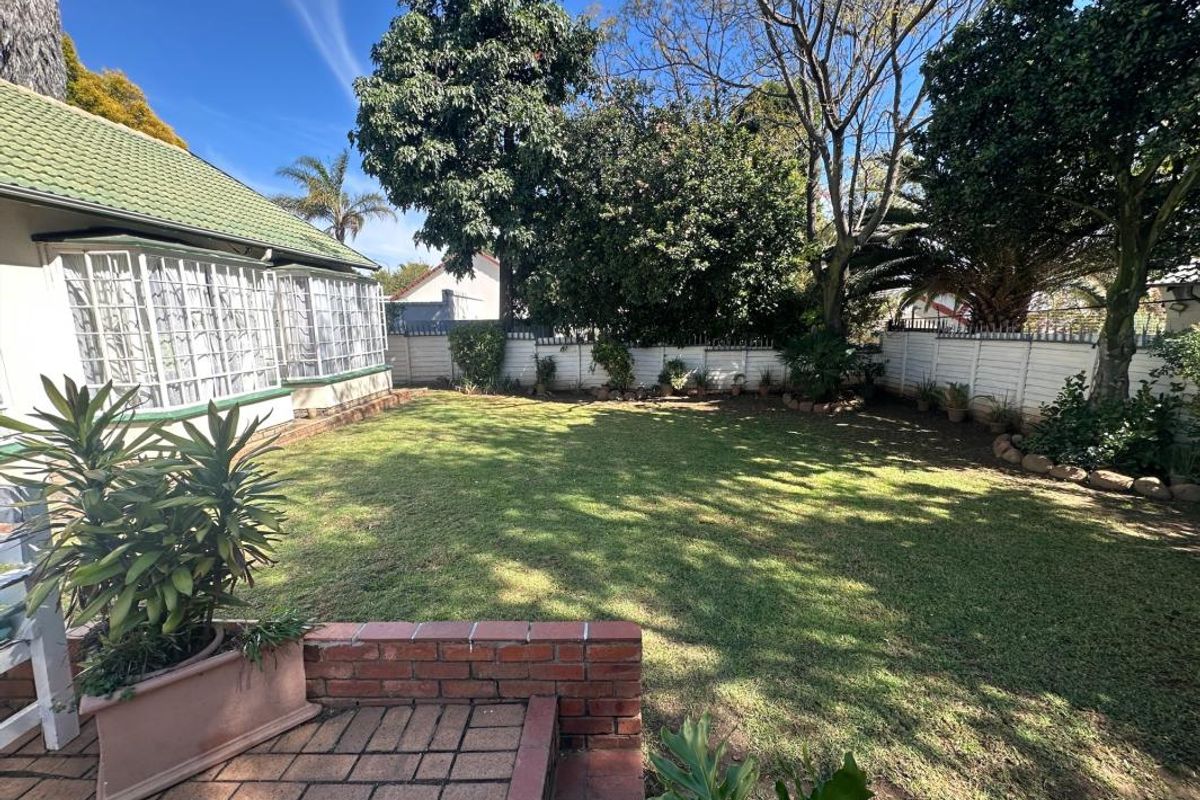 A well-maintained rear garden featuring a brick-paved patio, a lush lawn, and secure perimeter walling with established trees.