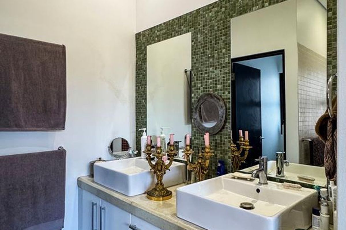 Modern bathroom featuring a double vanity with vessel sinks, stone countertop, and a decorative green mosaic tile backsplash.