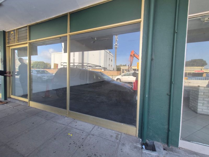 Front facade of a commercial property featuring large glass display windows with metal framing and a paved sidewalk entrance.