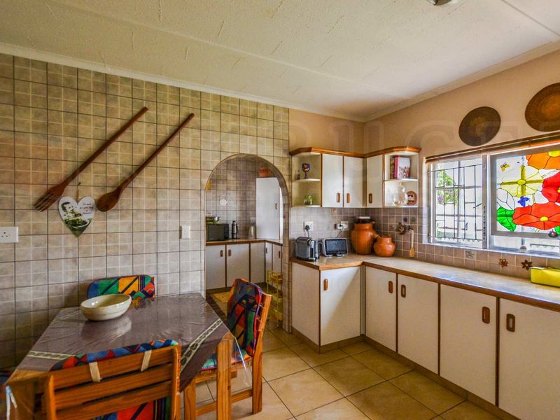 A functional kitchen featuring tiled splashbacks, built-in cabinetry, laminate countertops, and a distinctive stained glass window, with an adjoining scullery area.