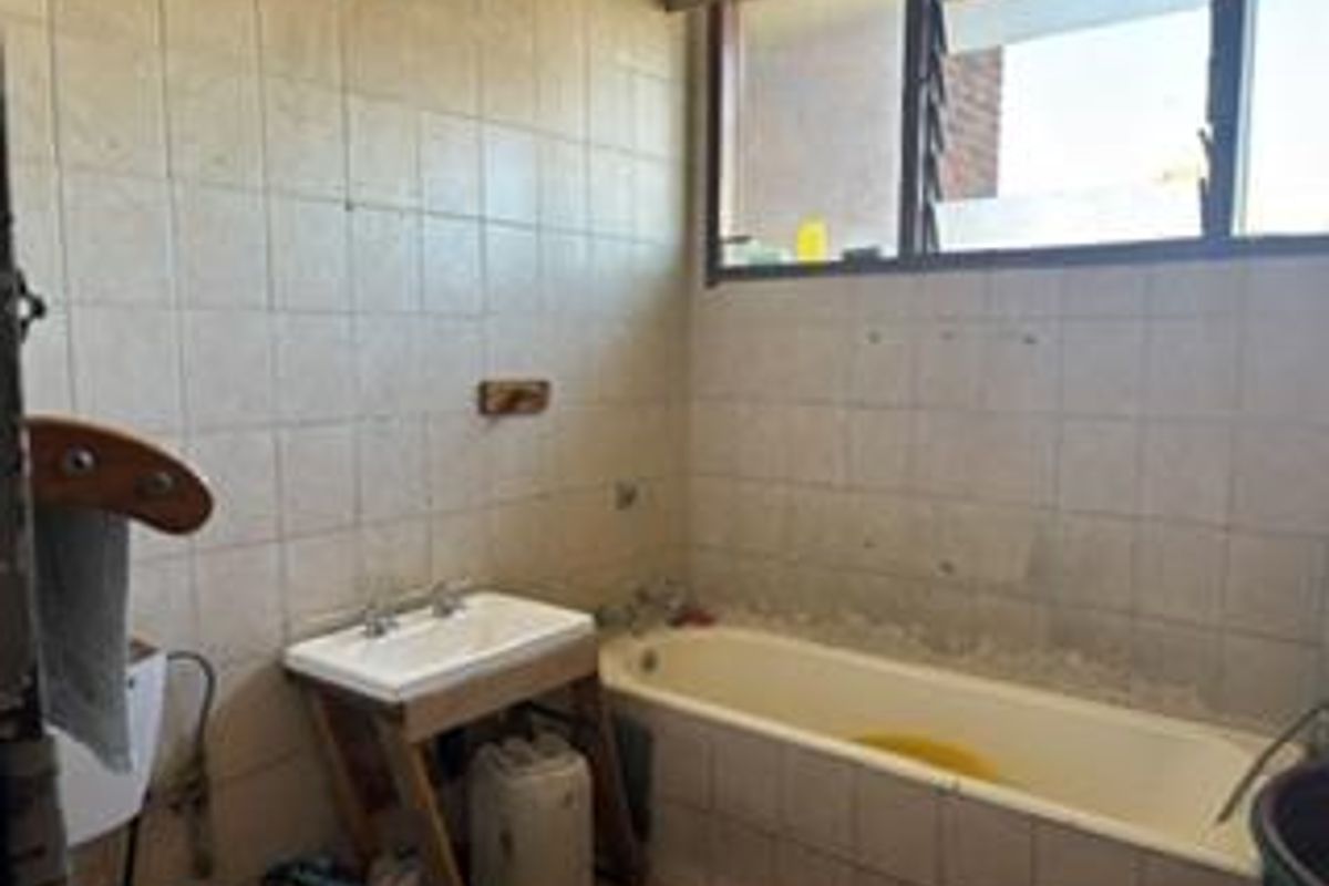 A dated bathroom featuring a built-in bathtub, wall-mounted basin, and tiled walls, requiring modernization and renovation of fixed finishes.