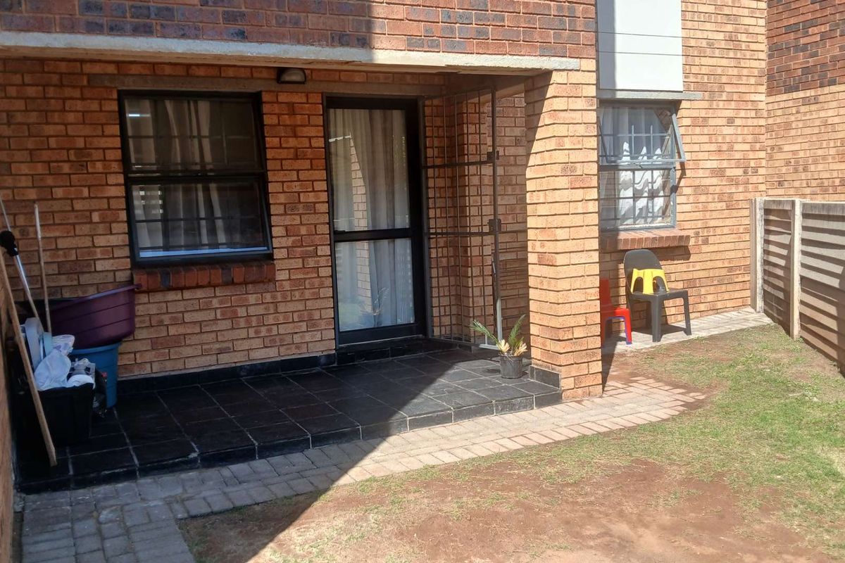 A rear exterior view of the apartment featuring a small tiled patio, brick facade, and a private garden area with a boundary wall.