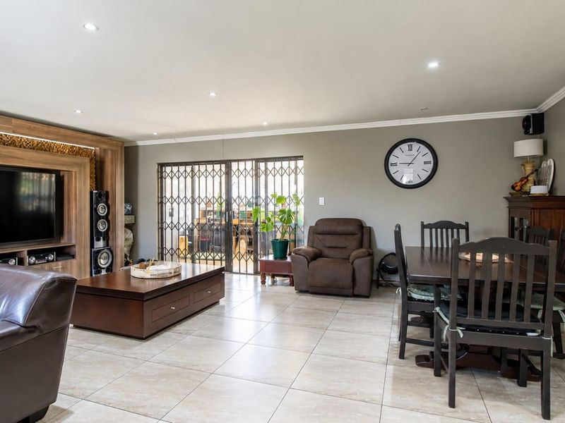 Spacious open-plan living and dining area featuring tiled flooring, recessed lighting, and a custom built-in media unit with direct access to the patio.