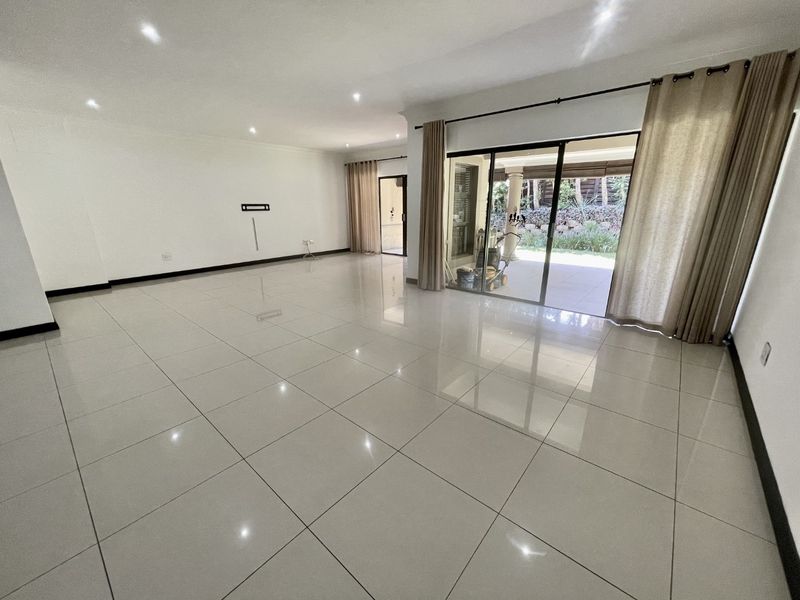 Spacious, light-filled living area featuring polished porcelain floor tiles, recessed downlighting, and large sliding glass doors providing seamless access to the outdoor patio.