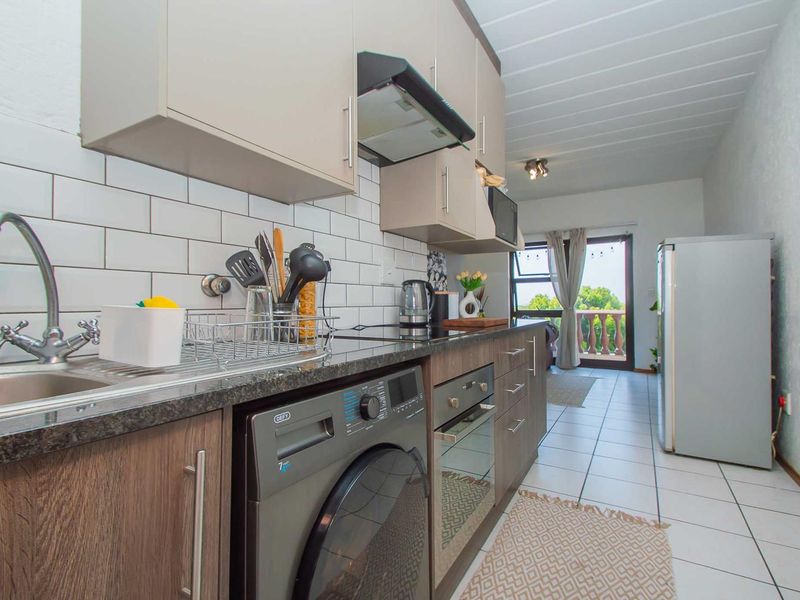 Modern galley-style kitchen featuring subway tile backsplash, granite countertops, built-in oven, extractor fan, and integrated laundry plumbing, leading to a balcony.