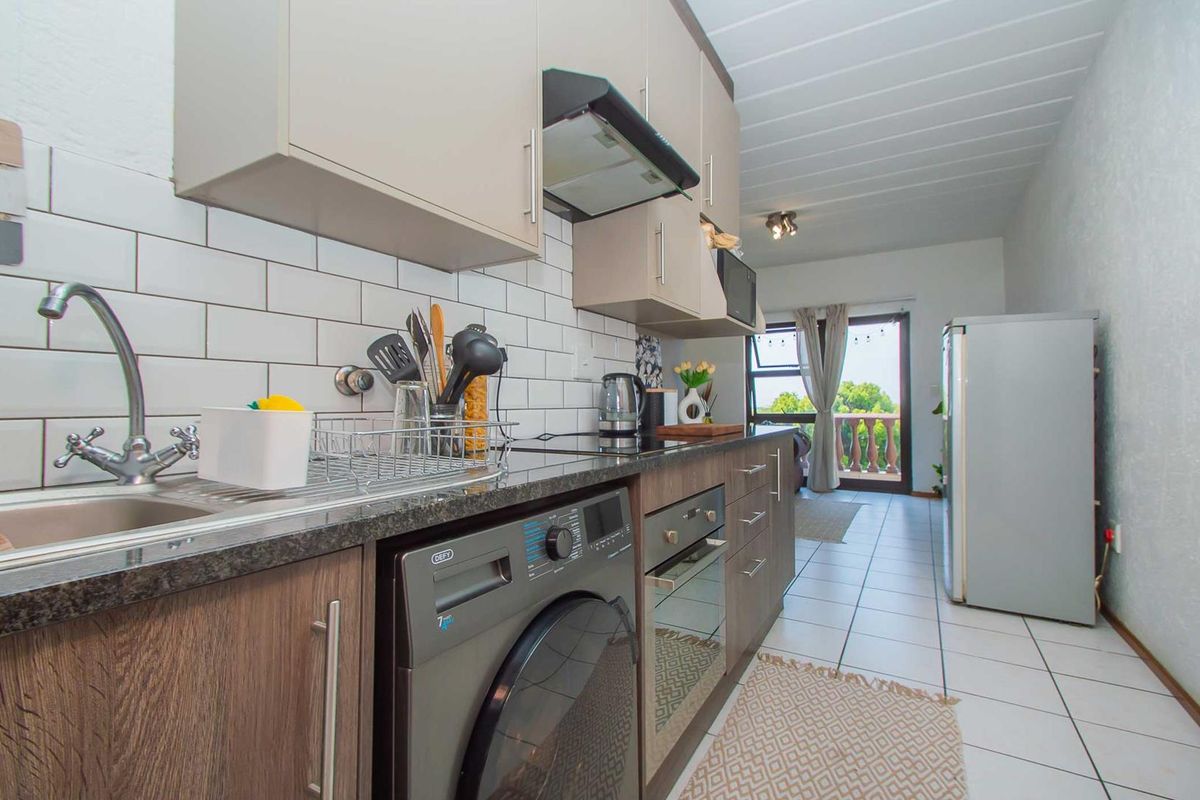 Modern galley-style kitchen featuring subway tile backsplash, granite countertops, built-in oven, extractor fan, and integrated laundry plumbing, leading to a balcony.