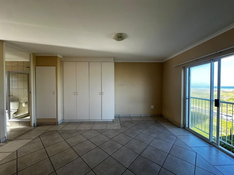 Spacious bedroom featuring tiled flooring, built-in cupboards, and a sliding glass door leading to a balcony with scenic coastal views.