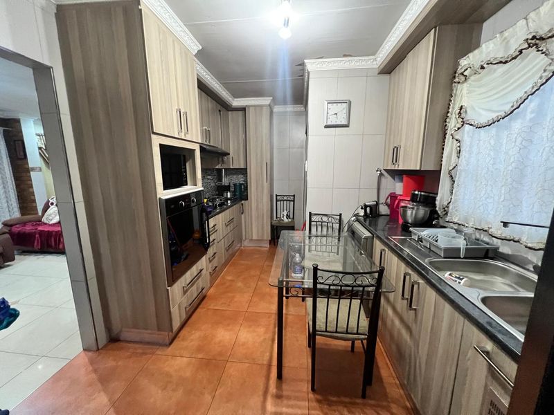 A functional kitchen featuring wood-look cabinetry, built-in oven, extractor fan, and double sink with tiled flooring.