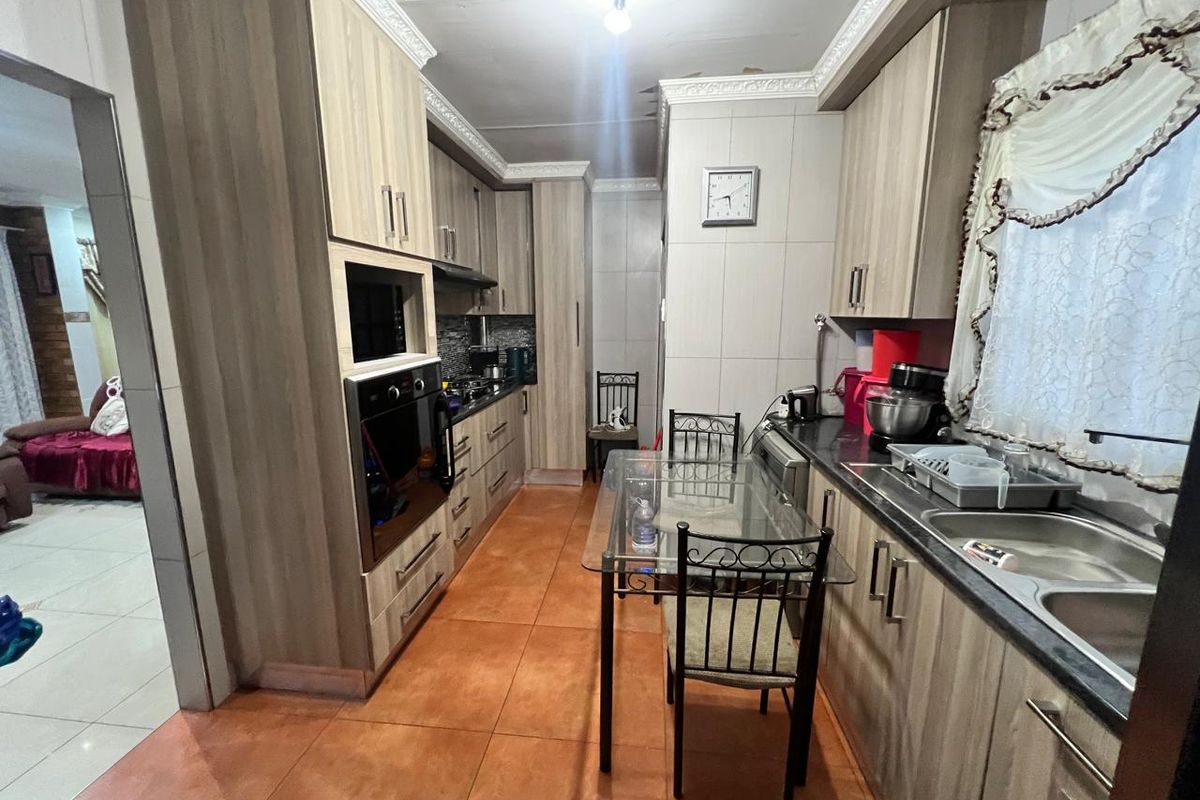 A functional kitchen featuring wood-look cabinetry, built-in oven, extractor fan, and double sink with tiled flooring.