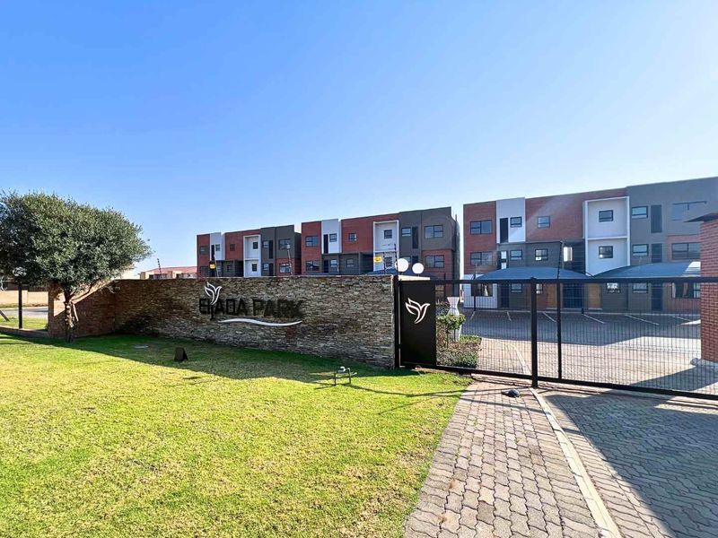 Front entrance view of the Elada Park apartment complex, featuring a stone-clad boundary wall, secure gated access, and well-maintained paved driveway and lawn.