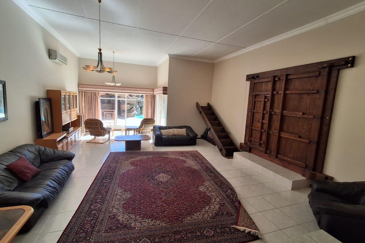 Spacious living room featuring tiled flooring, a decorative wooden wall feature, and large sliding glass doors providing access to the outdoor pool area.