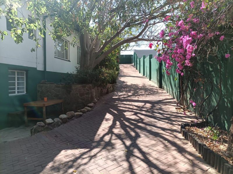 A paved driveway leading up a gentle slope, bordered by a stone retaining wall, mature trees, and perimeter fencing alongside the apartment building.