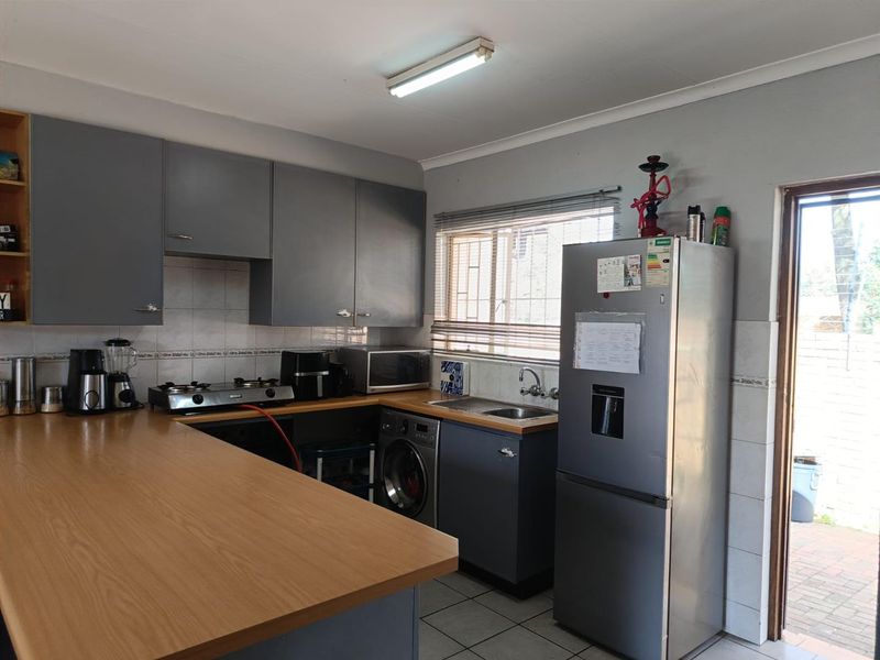 A functional kitchen featuring grey cabinetry, wooden countertops, tiled backsplash, and integrated laundry facilities with direct access to an outdoor area.
