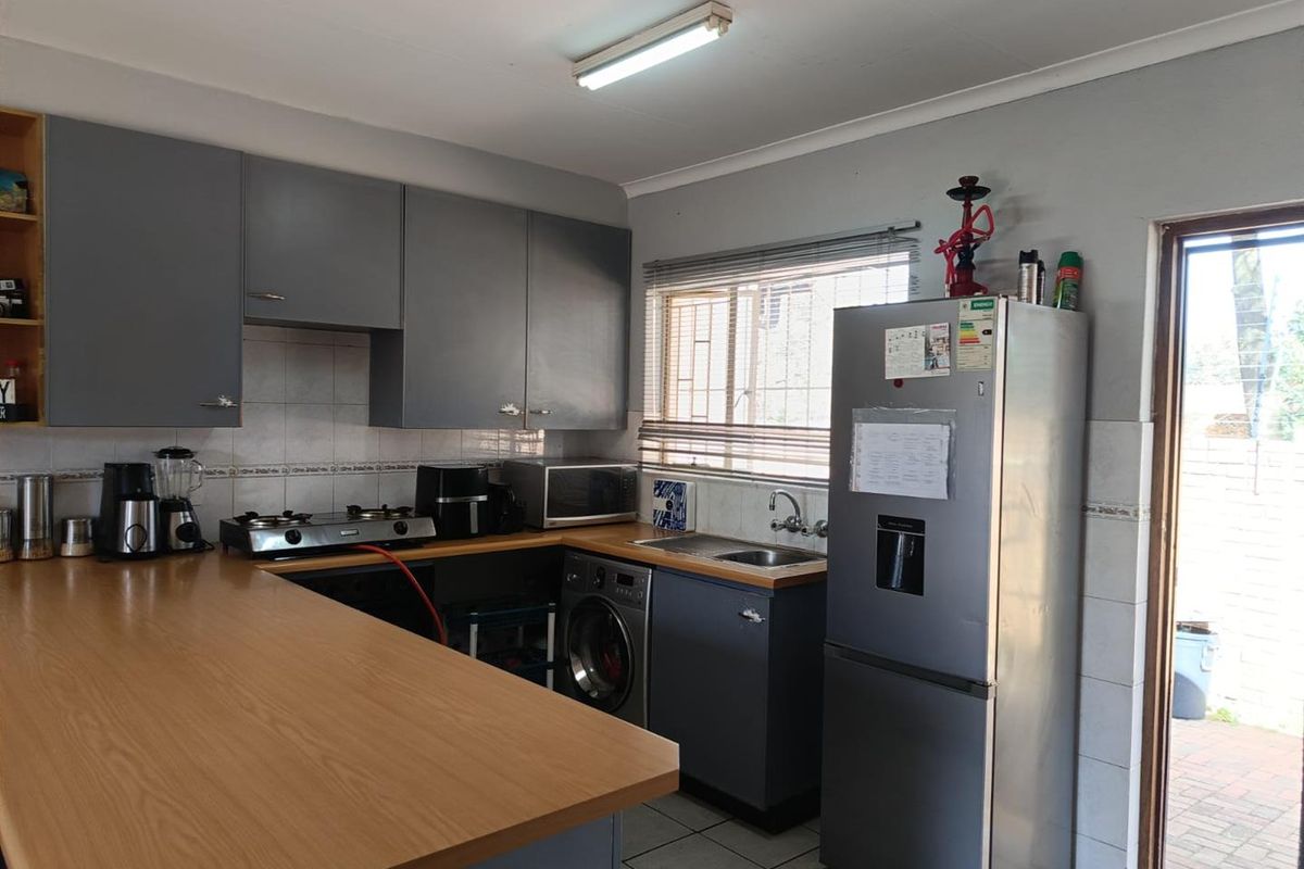 A functional kitchen featuring grey cabinetry, wooden countertops, tiled backsplash, and integrated laundry facilities with direct access to an outdoor area.