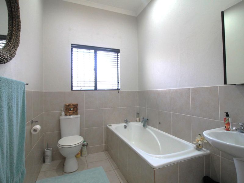 A functional bathroom featuring a bathtub, pedestal basin, and toilet with neutral wall and floor tiling.