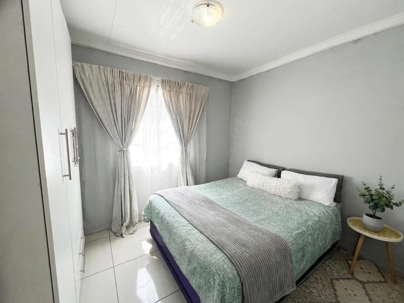A well-maintained bedroom featuring neutral grey walls, tiled flooring, and a built-in wardrobe with modern finishes.