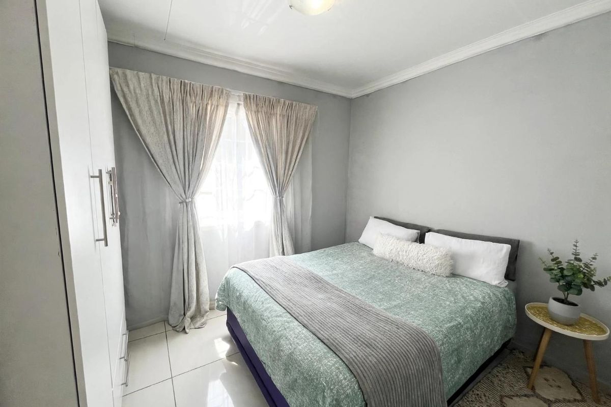 A well-maintained bedroom featuring neutral grey walls, tiled flooring, and a built-in wardrobe with modern finishes.