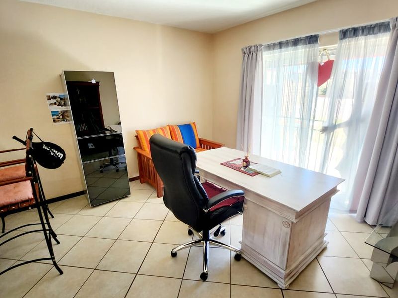 A functional home office space featuring tiled flooring and a large sliding glass door providing natural light and access to the exterior.