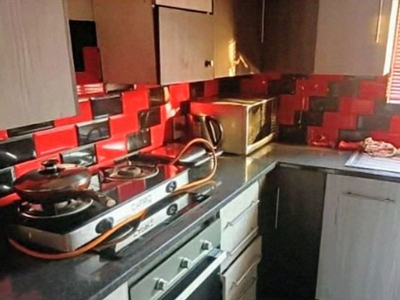 A compact kitchen featuring built-in cabinetry, a gas hob, an integrated oven, and a distinctive red and black tiled splashback.