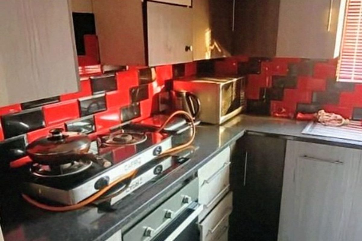 A compact kitchen featuring built-in cabinetry, a gas hob, an integrated oven, and a distinctive red and black tiled splashback.