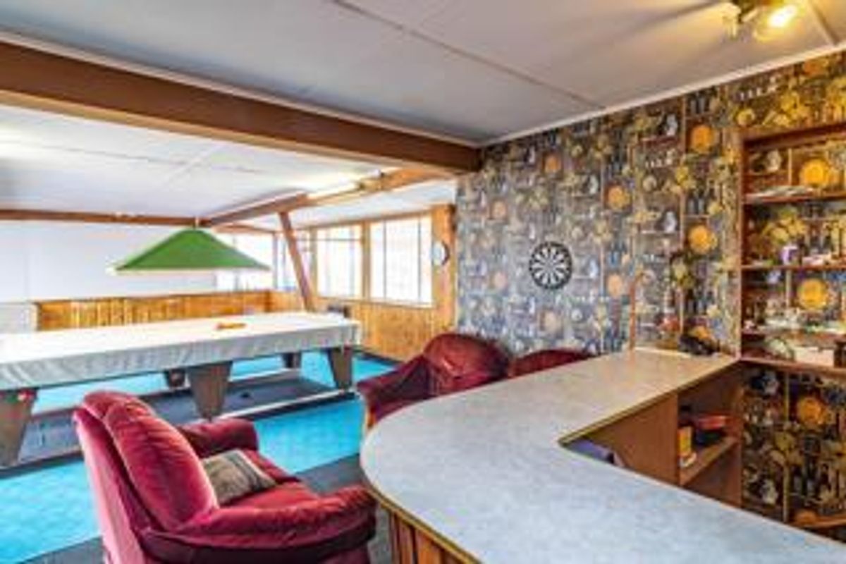A spacious entertainment room featuring a built-in bar, wood-paneled walls, and a dedicated area for a pool table.