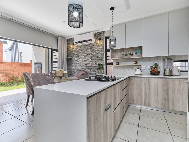 Modern open-plan kitchen and dining area featuring a central island with gas hob, stone-look feature wall, and seamless flow to the outdoor patio.